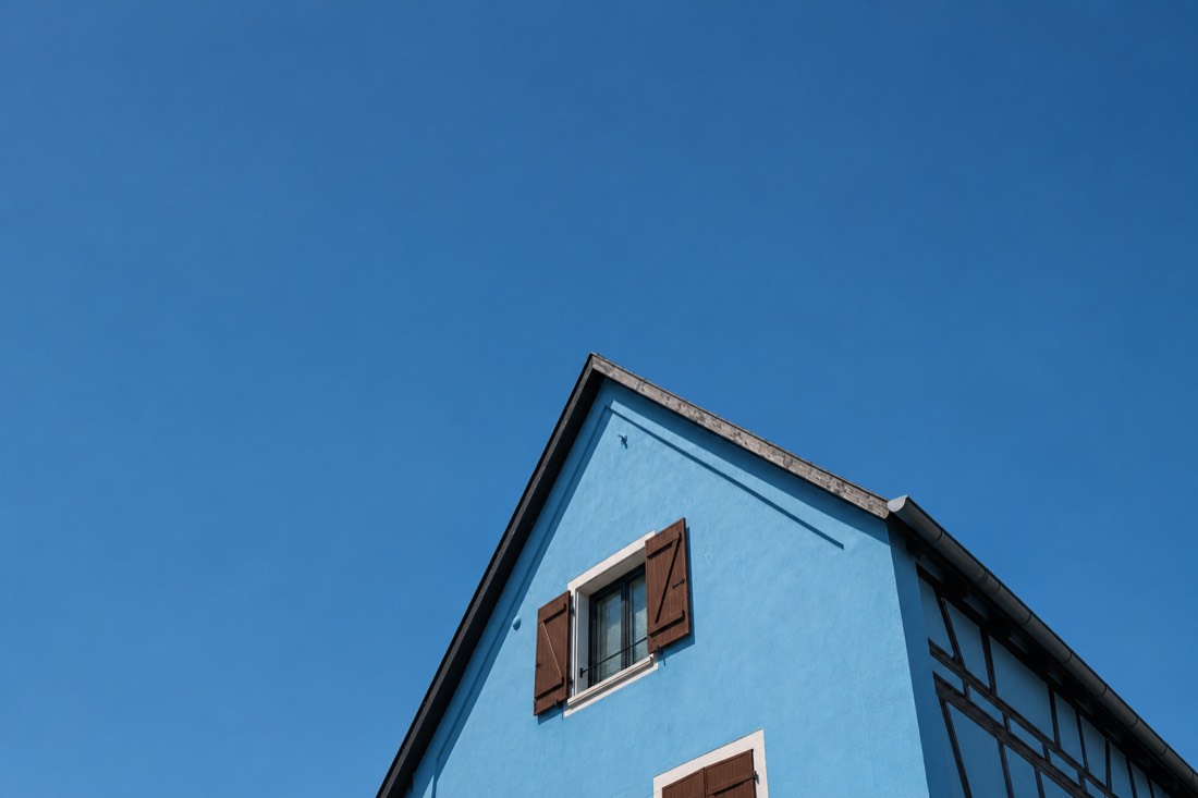 The gable of a blue house with brown shutters against a clear blue sky